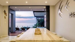 A modern dining area with a wooden table and chairs, a view of the outdoors, and a pergola structure. - Perfect Family Holiday Villa in Camps Bay Spindrift (Cape Town)