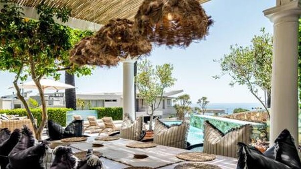 An outdoor dining area with round tables, leather chairs, and a view of a pool and greenery. - Magical Holiday Home Walking Distance to the Beach Sedgemoor Villa (Cape Town)