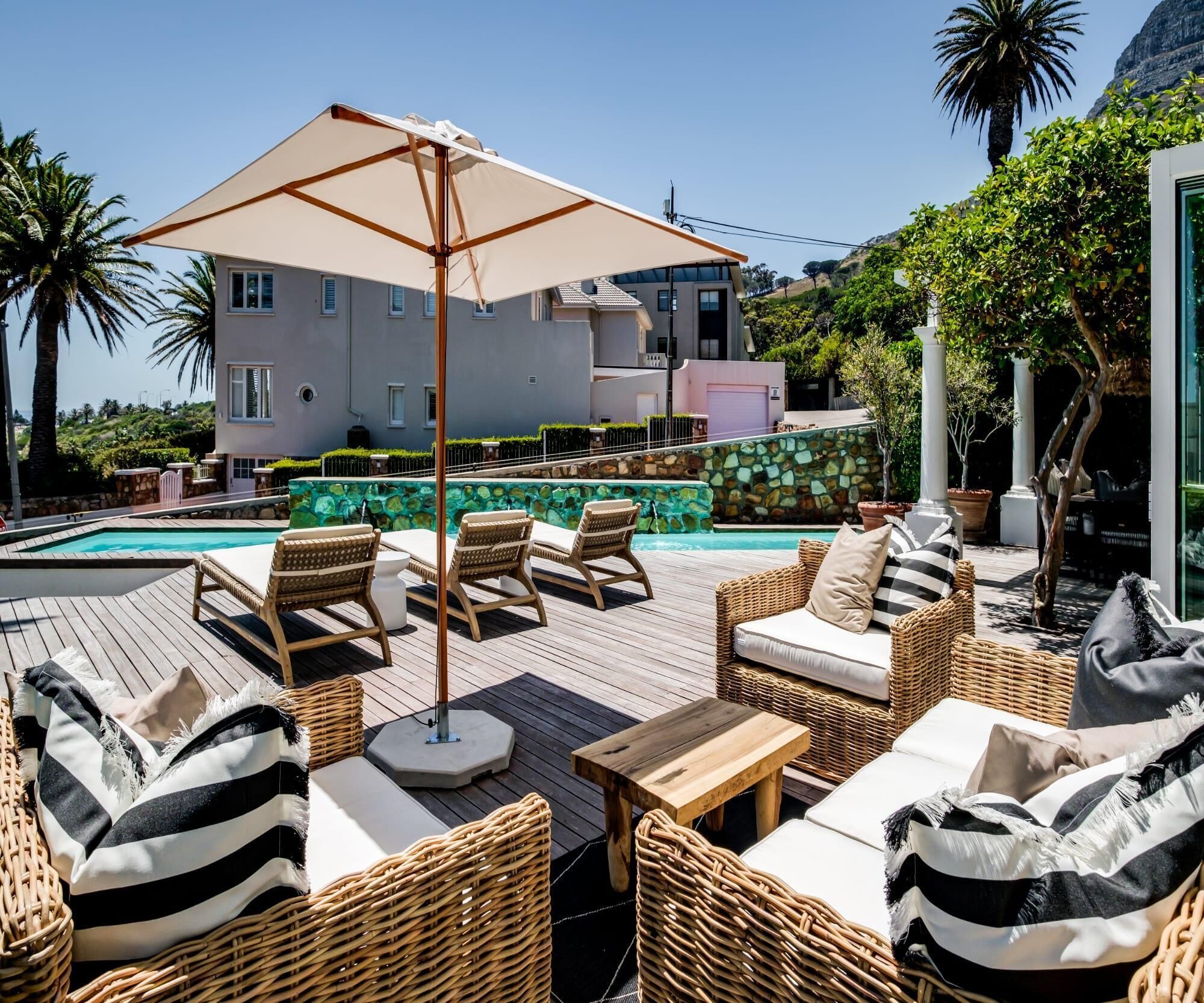 Un espace aménagé au bord de la piscine, avec des meubles en osier, un grand parasol et un mur en pierre.