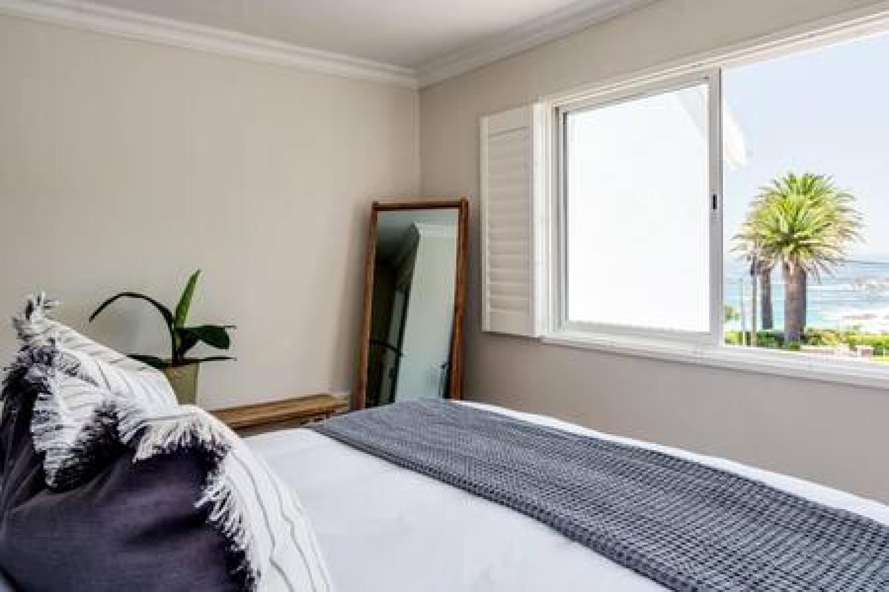 Un dormitorio con cama, ventana con vista al mar, una planta y un espejo.