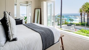 A bedroom with a large bed, a view of the ocean, and a balcony with palm trees. - Magical Holiday Home Walking Distance to the Beach Sedgemoor Villa (Cape Town)
