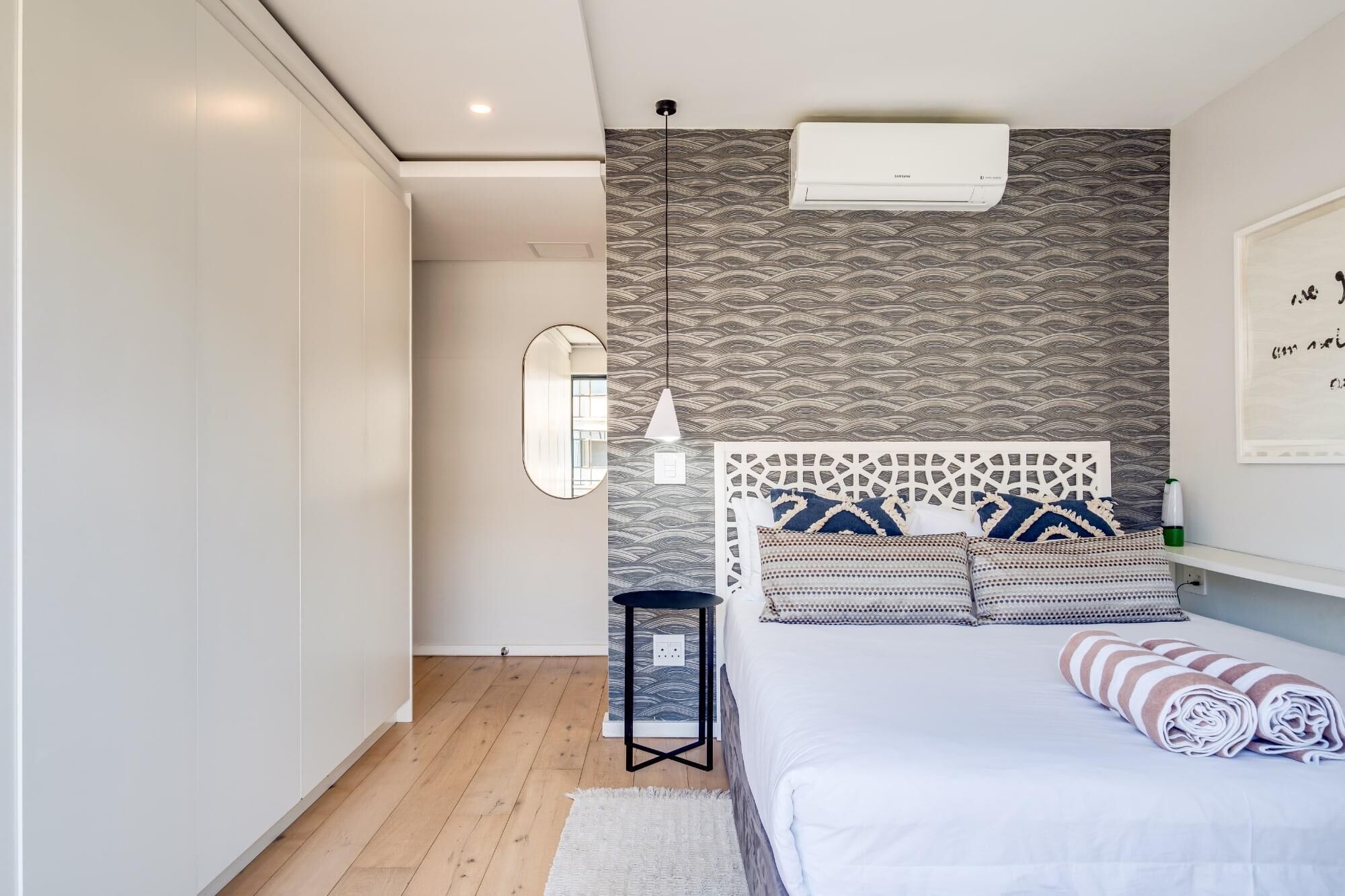 Une chambre à coucher comprenant un lit, une table de chevet, un miroir et un climatiseur fixé au mur.