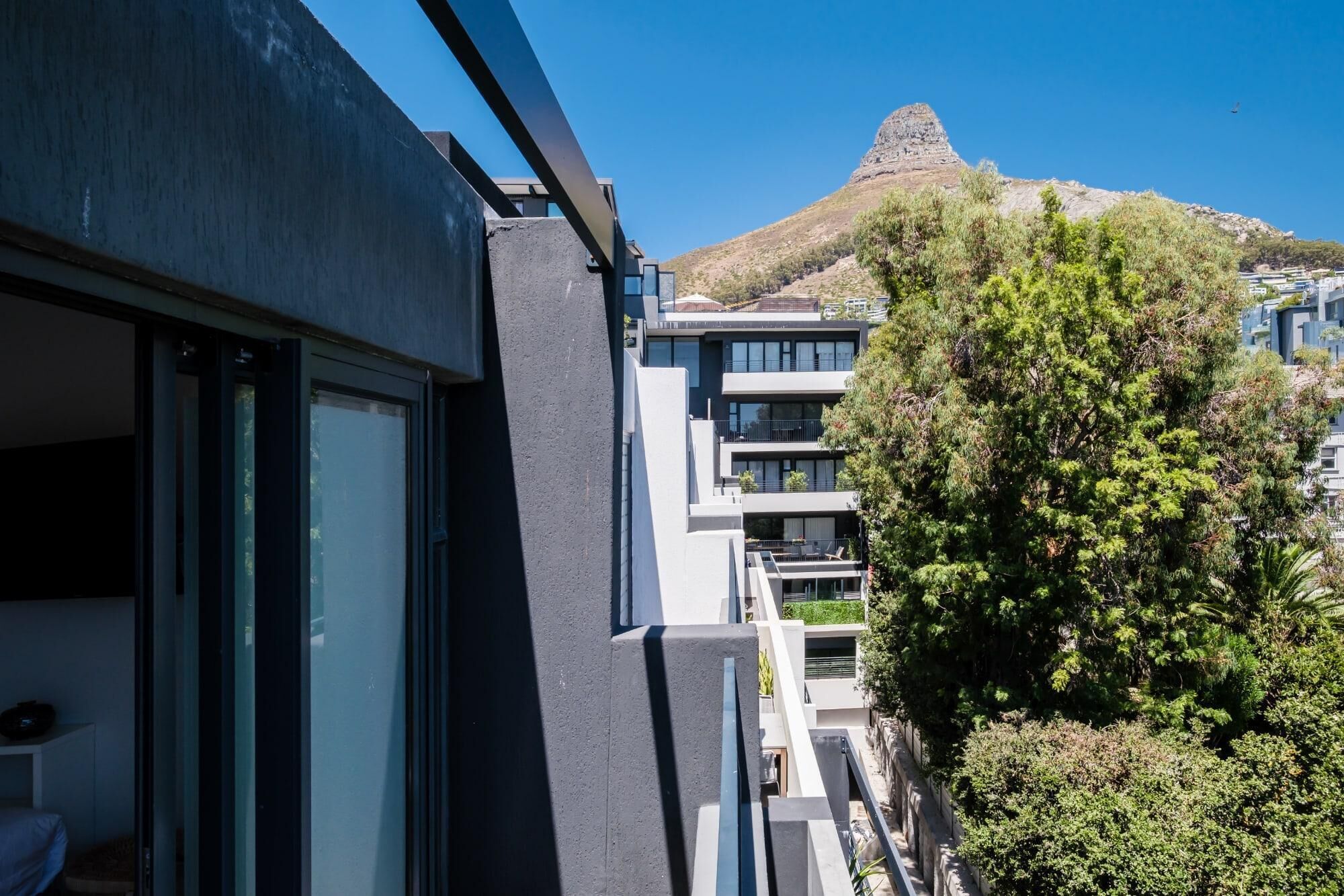 A modern building with balconies, a mountain in the background, and lush greenery.