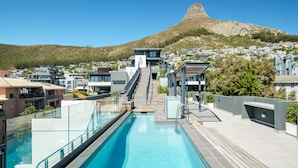 Un hôtel moderne doté d’une piscine, d’un escalier menant à une terrasse sur le toit et offrant une vue sur une montagne.