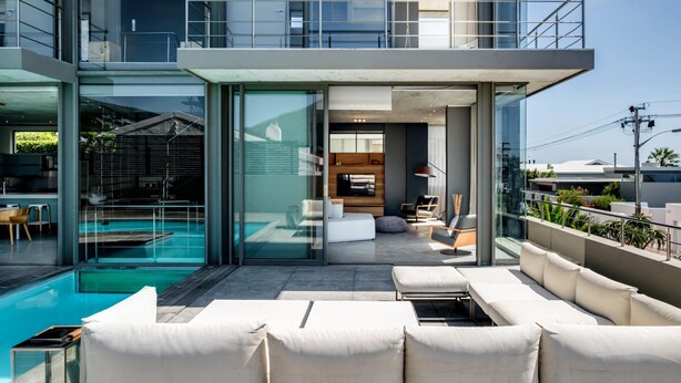Ein moderner Außenbereich mit Pool, Sitzgelegenheiten und einem Wintergarten, der zum Küchenbereich führt.