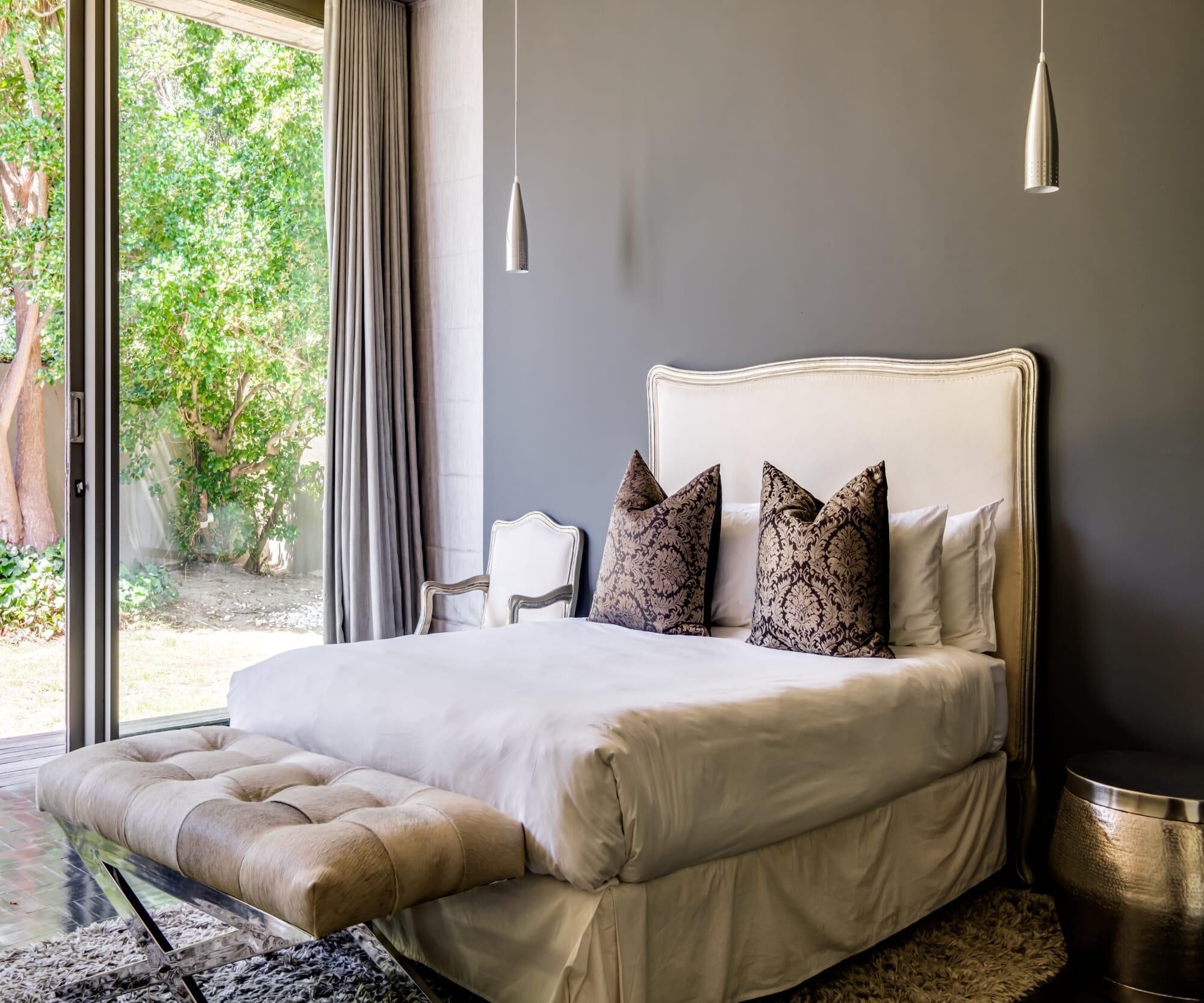 Ein Schlafzimmer mit einem großen Bett, einem Sessel und Blick auf Grünflächen.