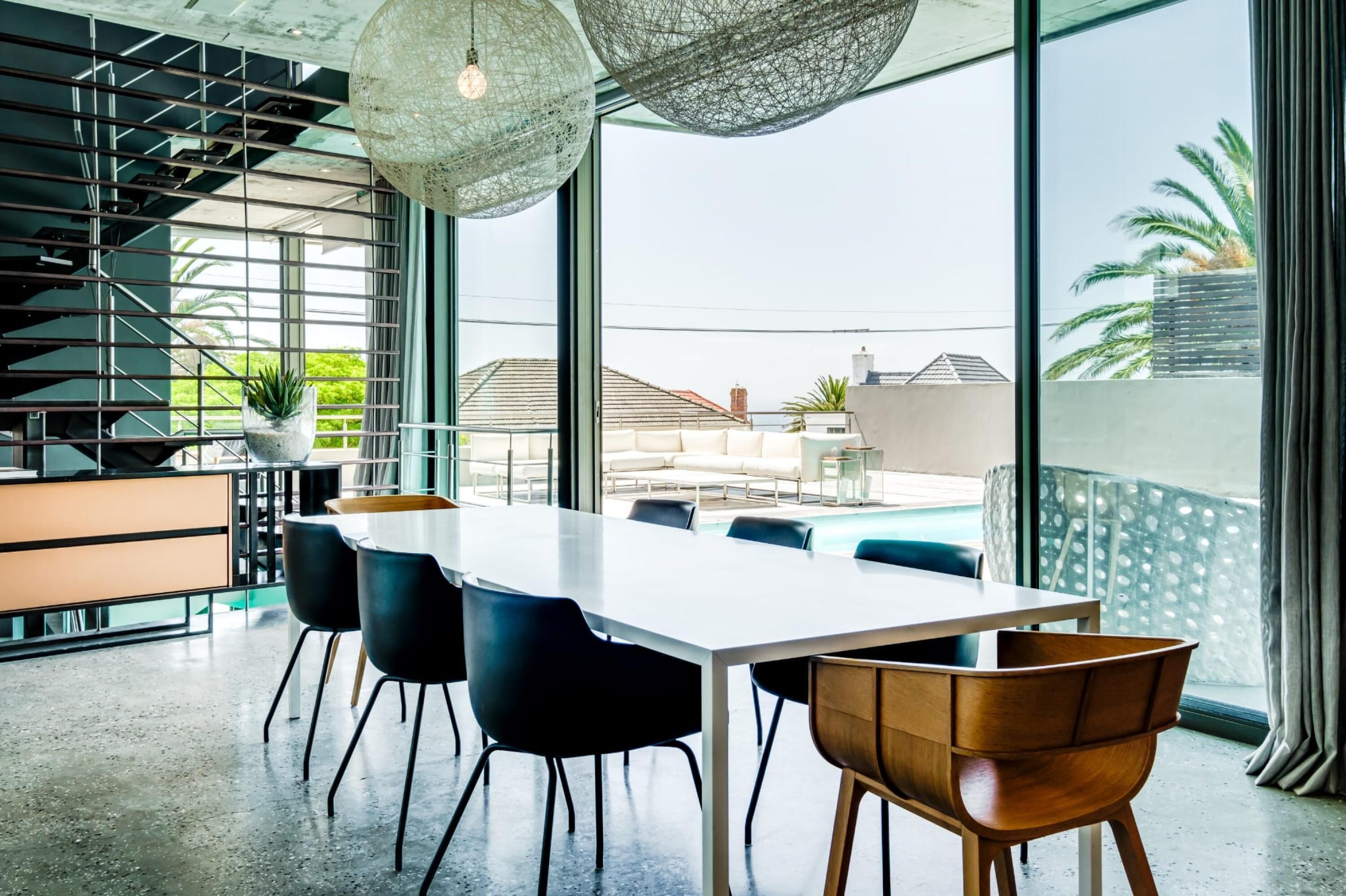 Un espace de salle à manger moderne, avec une grande table, des chaises noires et en bois, et un luminaire suspendu.