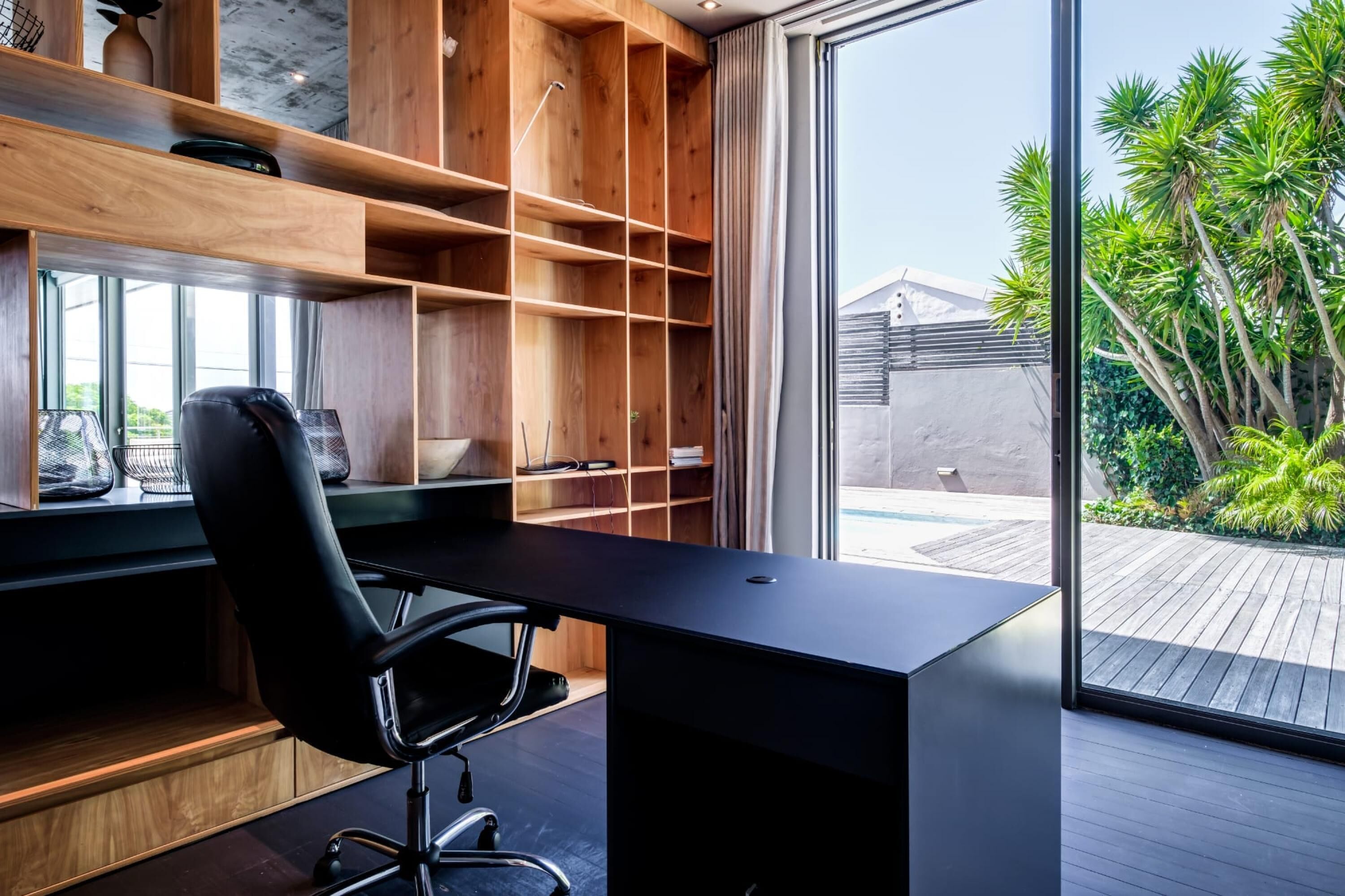 A modern office space with a wooden desk, black office chair, and built-in shelving.