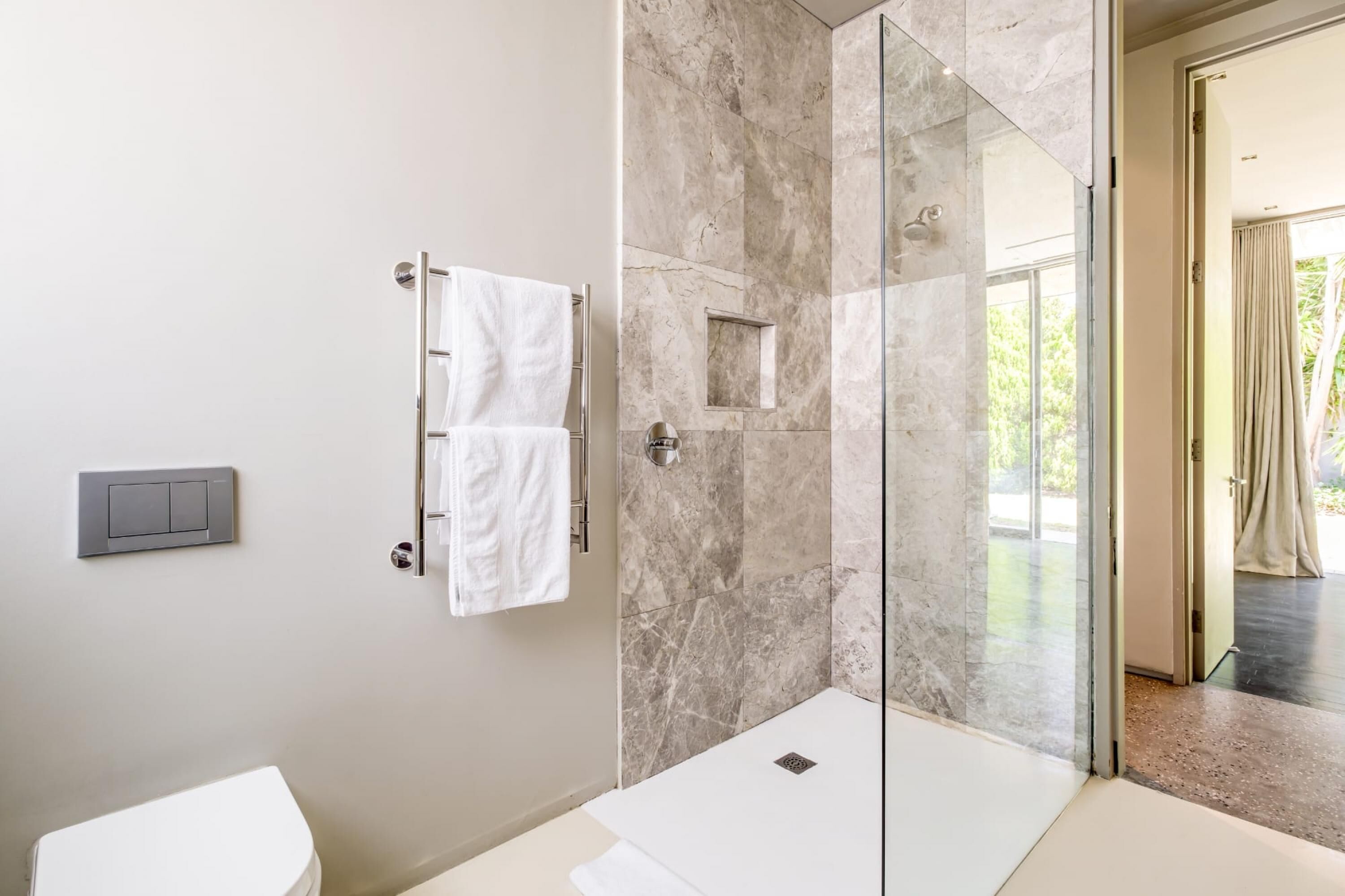 A modern bathroom with a glass-enclosed shower, marble walls, and a visible toilet.