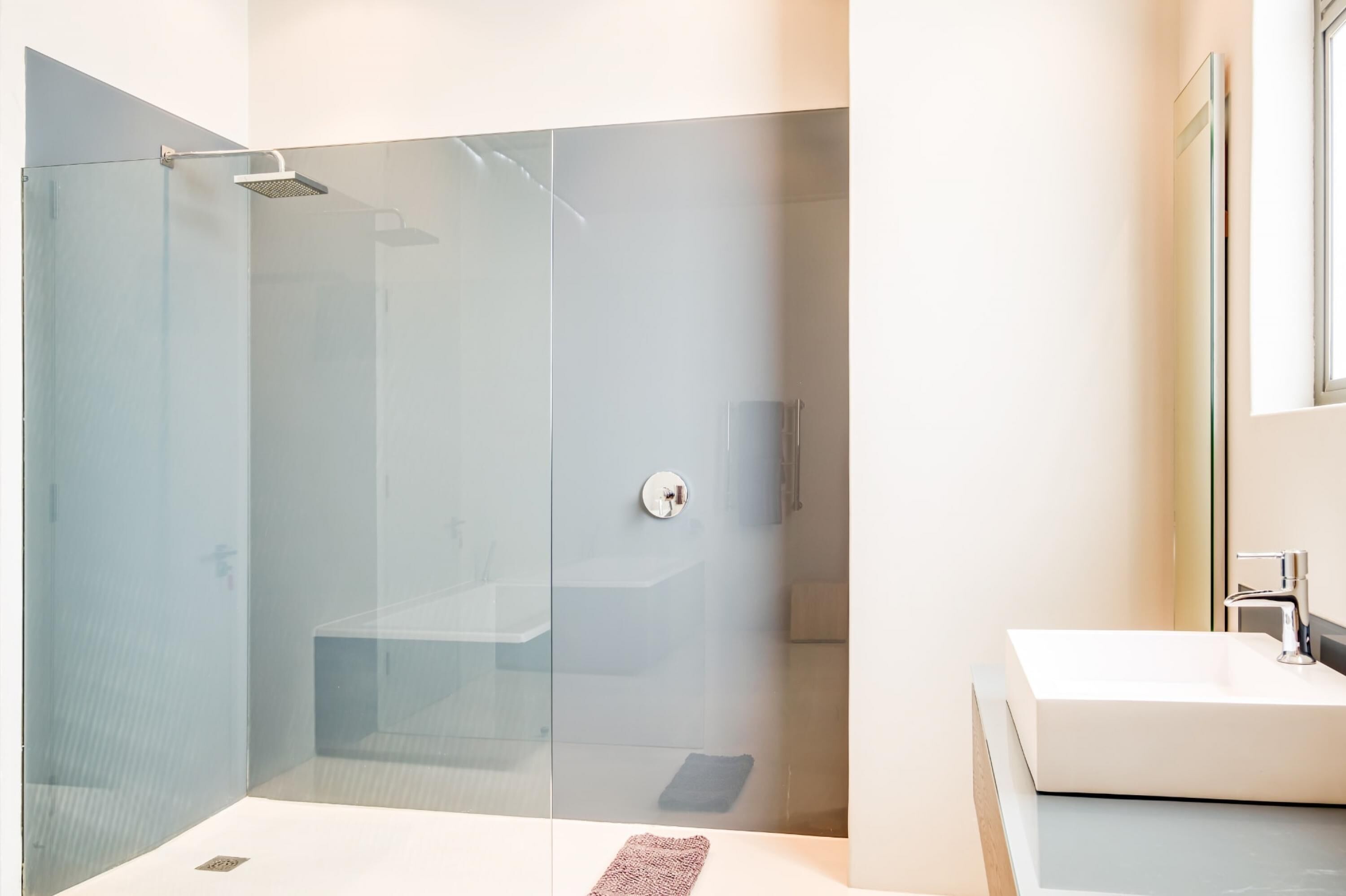 A modern bathroom with a glass-enclosed shower, a white sink, and a large mirror.