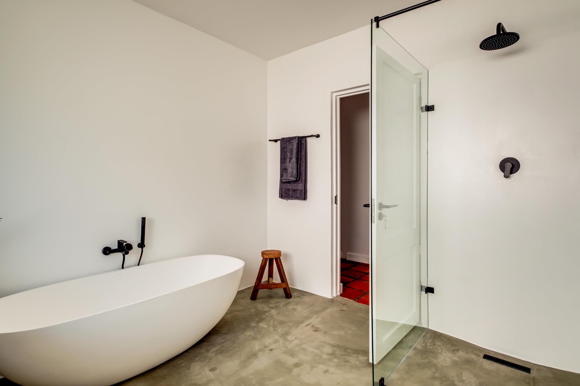 A modern bathroom with a freestanding bathtub, a glass shower enclosure, and a wooden stool.