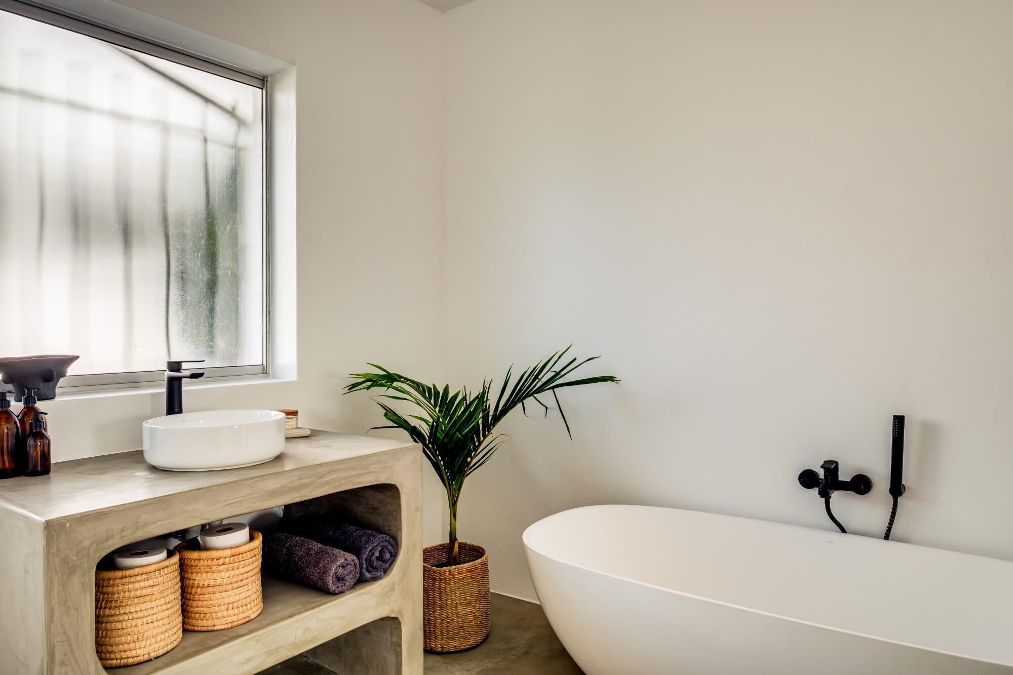Une salle de bain moderne avec une baignoire sur pieds, une grande fenêtre, un meuble-lavabo en bois et une plante en pot.