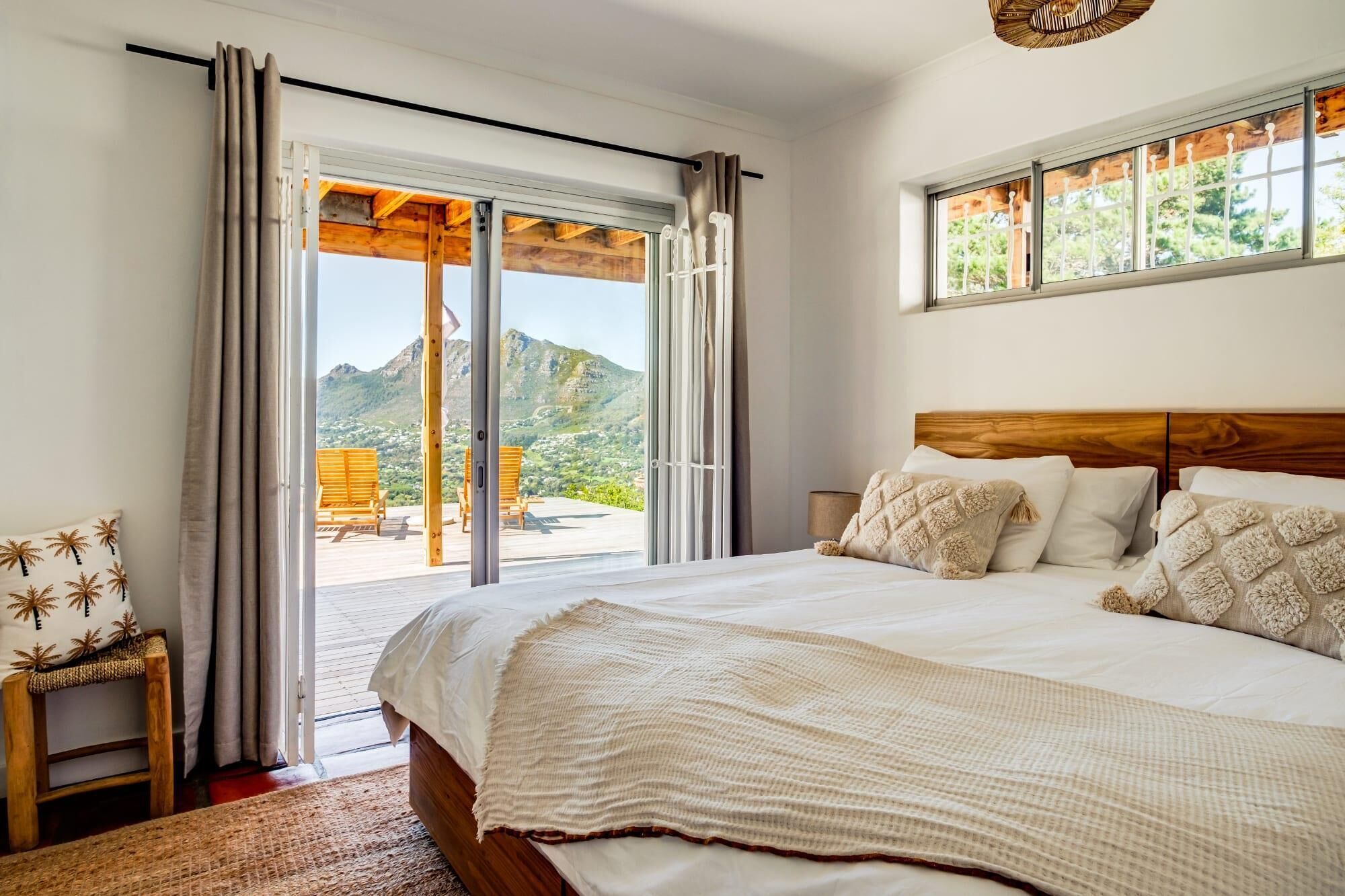 Une chambre à coucher avec un grand lit, une tête de lit en bois et une vue sur un paysage montagneux, visible à travers une porte-fenêtre coulissante.