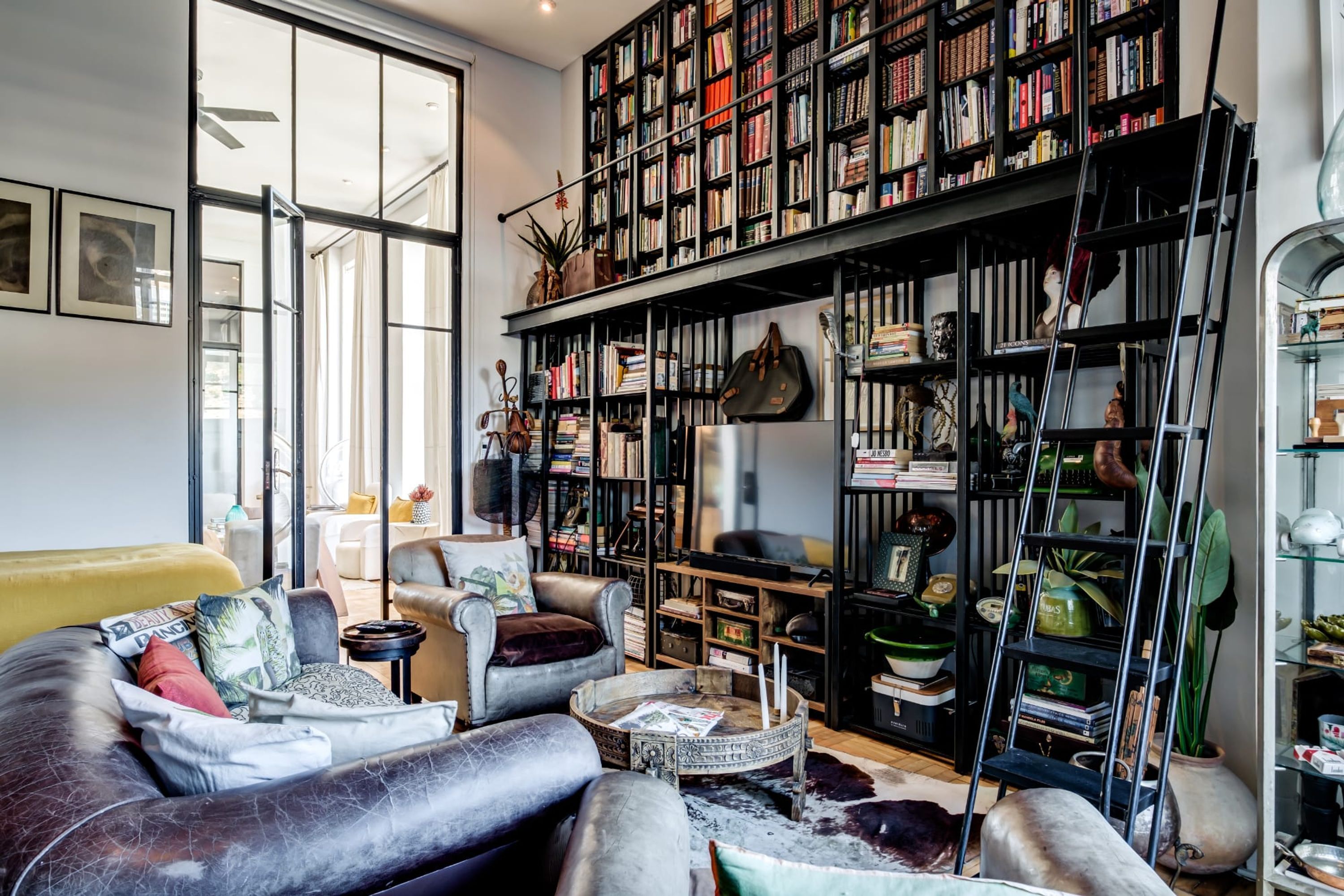 A cozy living room with a leather sofa, a coffee table, and a bookshelf filled with books and decorative items.
