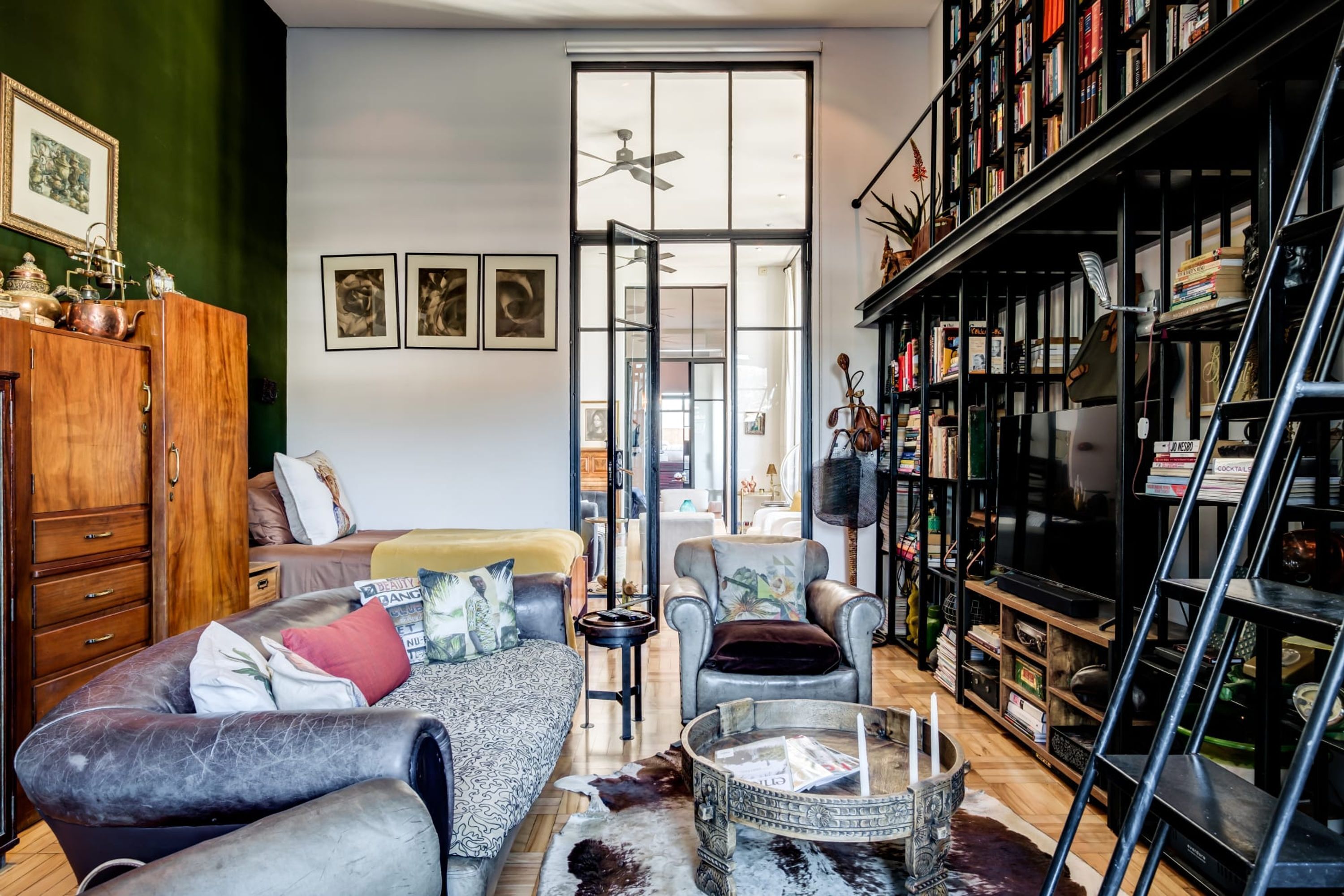 Een gezellige woonkamer met een bank, fauteuils, een salontafel en een boekenplank vol boeken en decoratieve objecten.