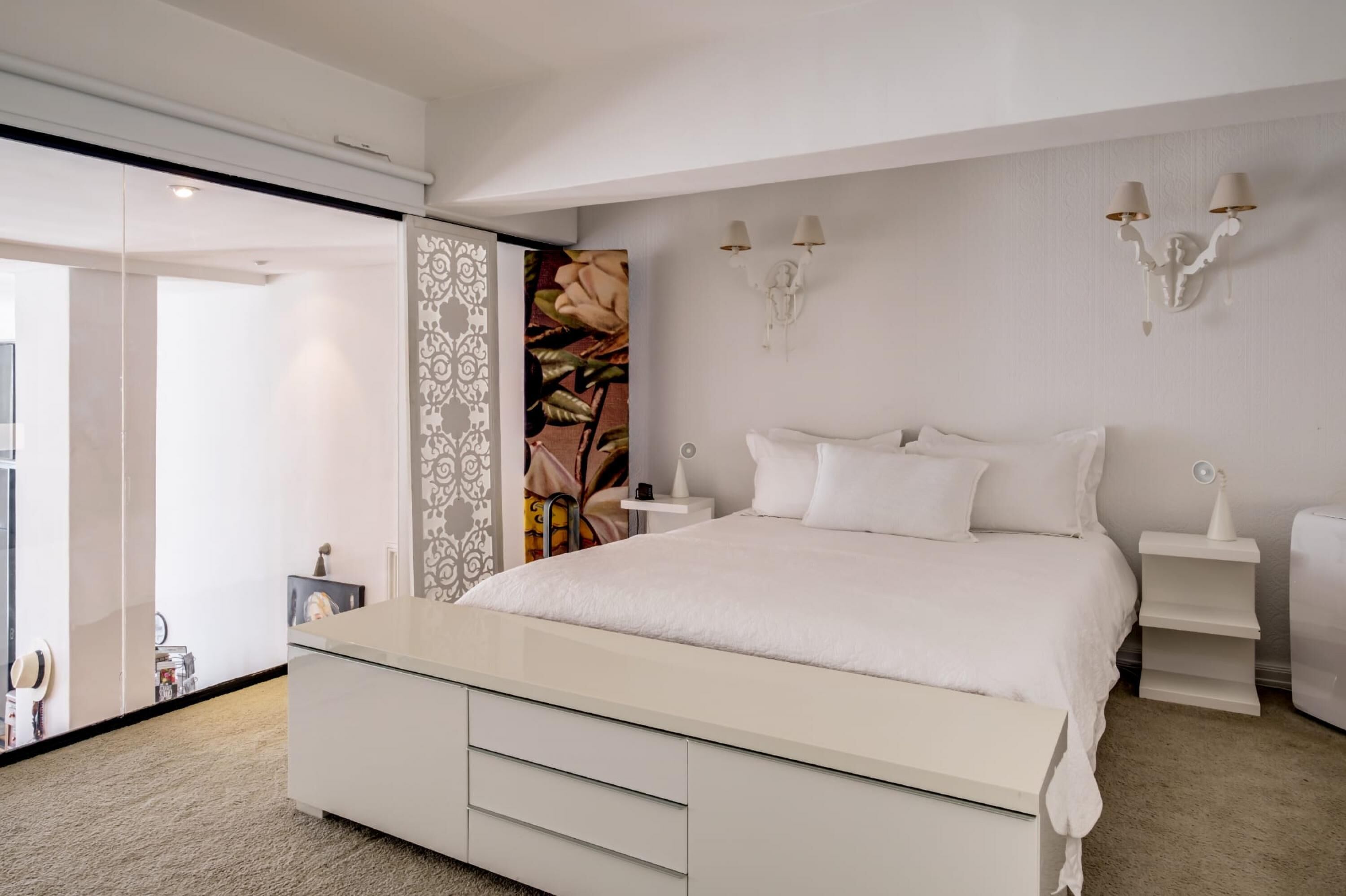 A modern bedroom with a large bed, a bedside table, a nightstand, and a wall-mounted lamp.