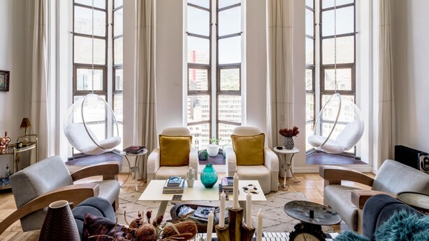 A modern living room with a large window, two white sofas with yellow cushions, a coffee table with books and candles, and a hanging chair. - Art Deco Loft in the Heart of Cape Town Splendid Loft (Cape Town)