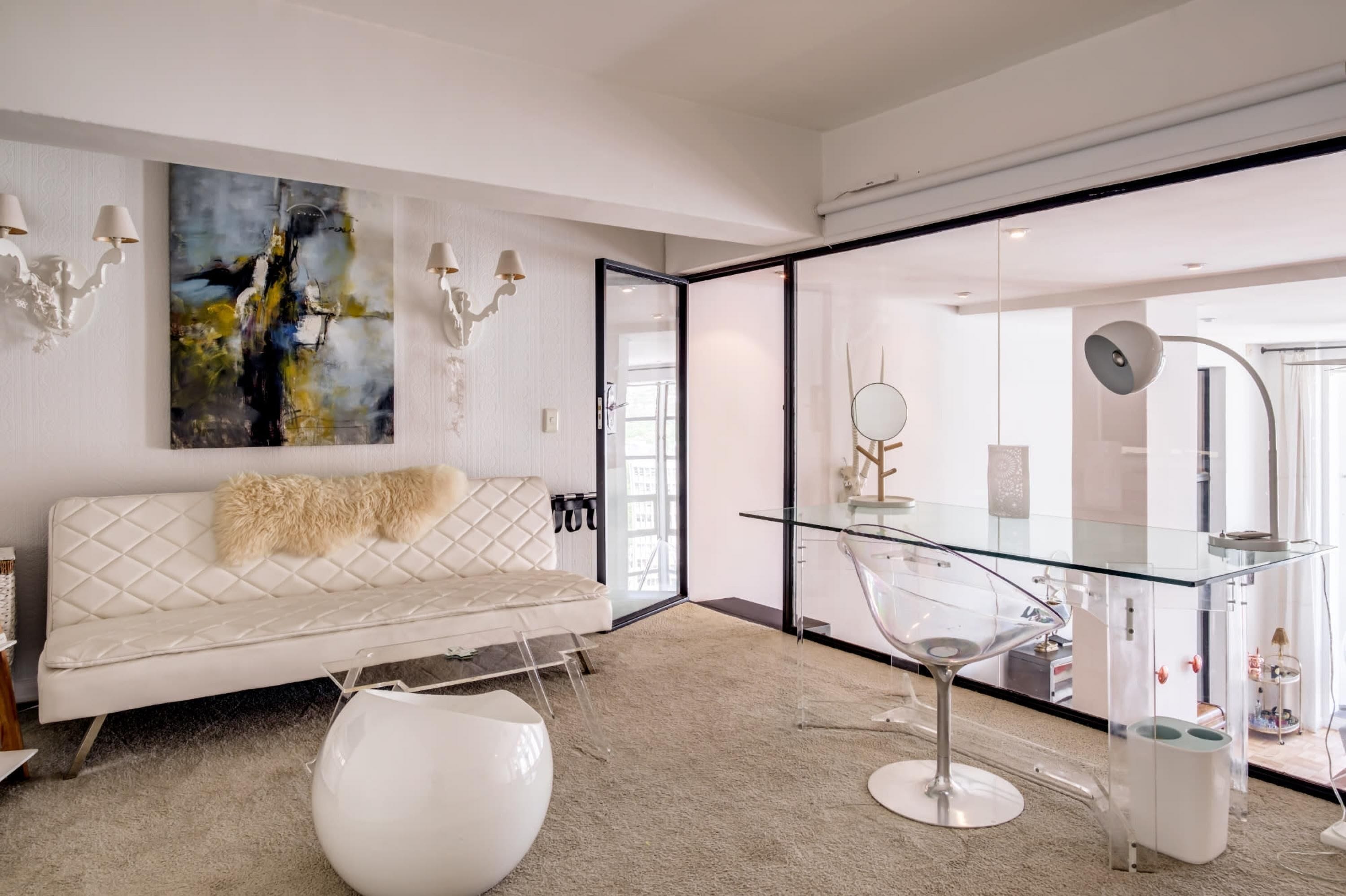 Un salon moderne avec un canapé blanc, des œuvres d’art abstraites et une table basse en verre.