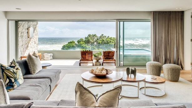 Ein modernes Wohnzimmer mit einem großen Fenster mit Blick auf den Ozean, möbliert mit einer Couch, Sesseln und einem Couchtisch.