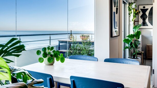 Un espace repas moderne avec vue sur l’océan, comprenant une table, des chaises et des plantes en pot.