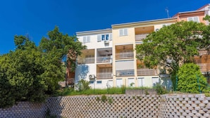 A multi-story residential building with balconies, a parking area, and a stone wall. - Holiday apartment with dishwasher and washing machine (Selce)