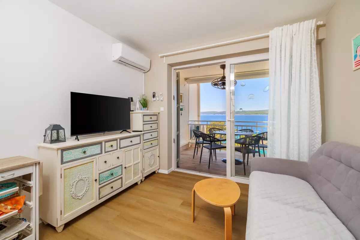 Un salon équipé d’un téléviseur, d’un canapé et offrant une vue sur la mer grâce à une porte coulissante.