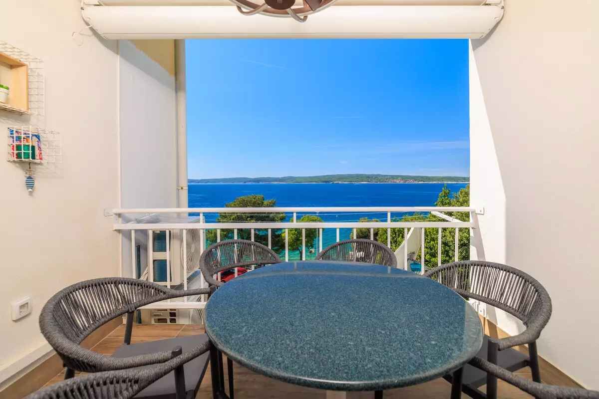 A balcony with a round table and chairs, overlooking a coastal view.