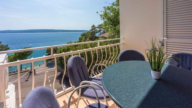 A balcony with a table and chairs, overlooking a body of water and greenery. - Holiday apartment with dishwasher and washing machine (Selce)