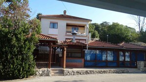 A two-story building with a balcony, a covered outdoor area, and a stone wall. - Holiday apartment with air conditioning (Crikvenica)