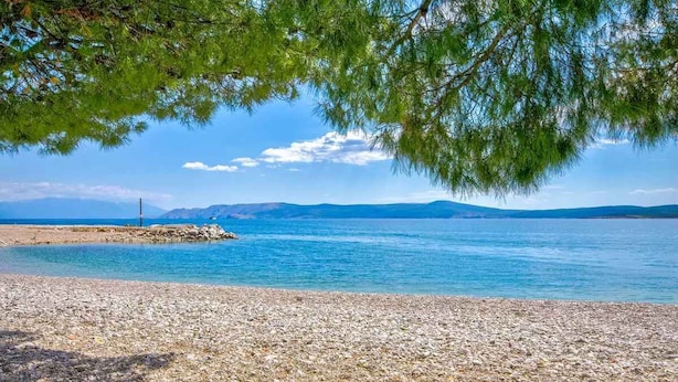 A pebble beach with clear blue water and distant mountains.