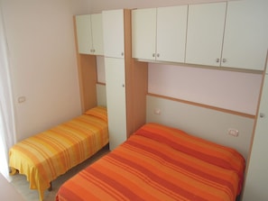 A room with two beds, each with striped bedding, and white cabinets above.