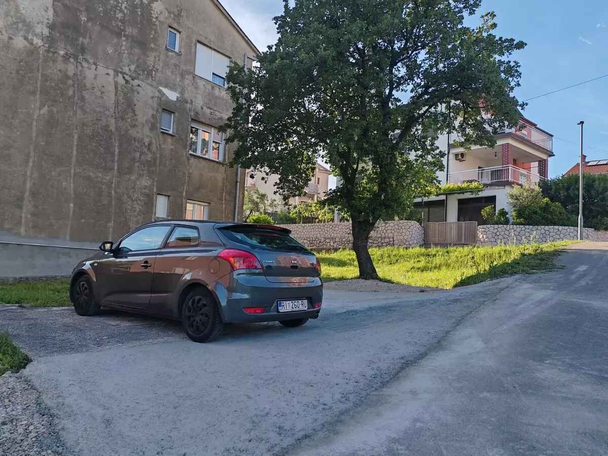 Ein Auto auf einer asphaltierten Straße, im Hintergrund ein Gebäude und ein Baum.