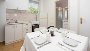 A compact kitchen with white cabinets, a built-in oven, and a dining area set for four with white tableware. - Studio with terrace and air conditioning (Crikvenica)