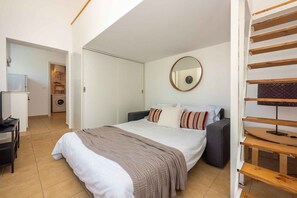 Relax in a serene bedroom with a large bed, round mirror, and comfortable desk area.