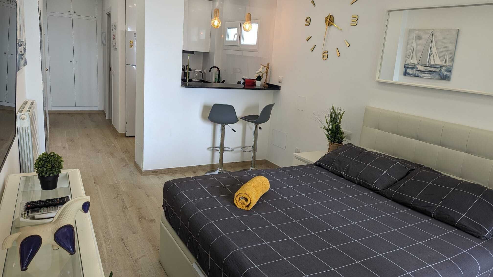 A modern bedroom with a bed, a small desk, and a kitchenette.