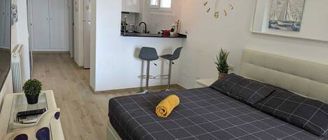 A modern bedroom with a bed, a small desk, and a kitchenette.