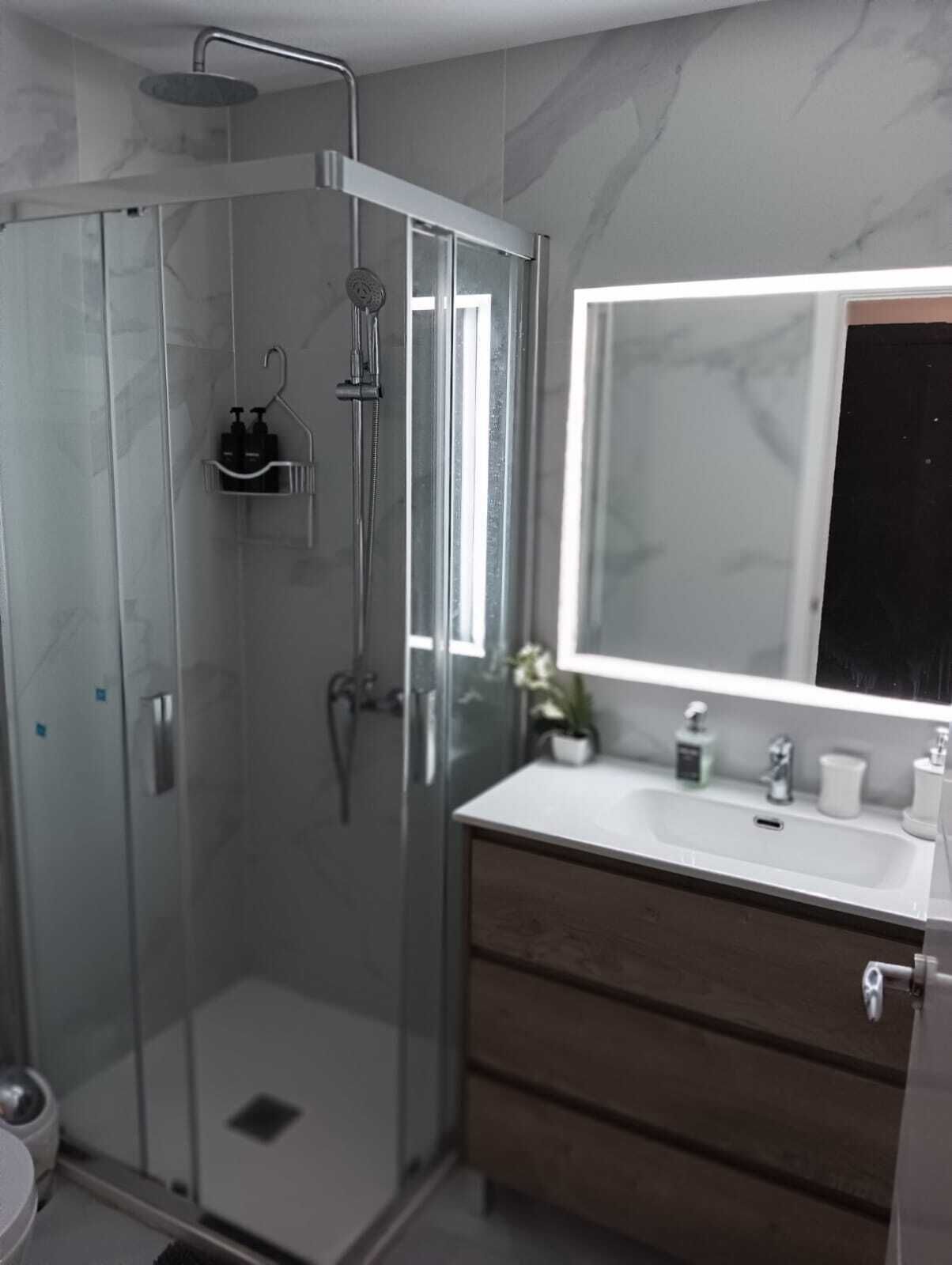 A modern bathroom with a glass-enclosed shower, a white sink, a mirror, and a dark wooden vanity.