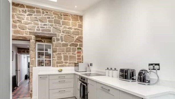 Une cuisine moderne avec des murs en pierre, des meubles blancs et un parquet en bois disposé en motif chevrons.