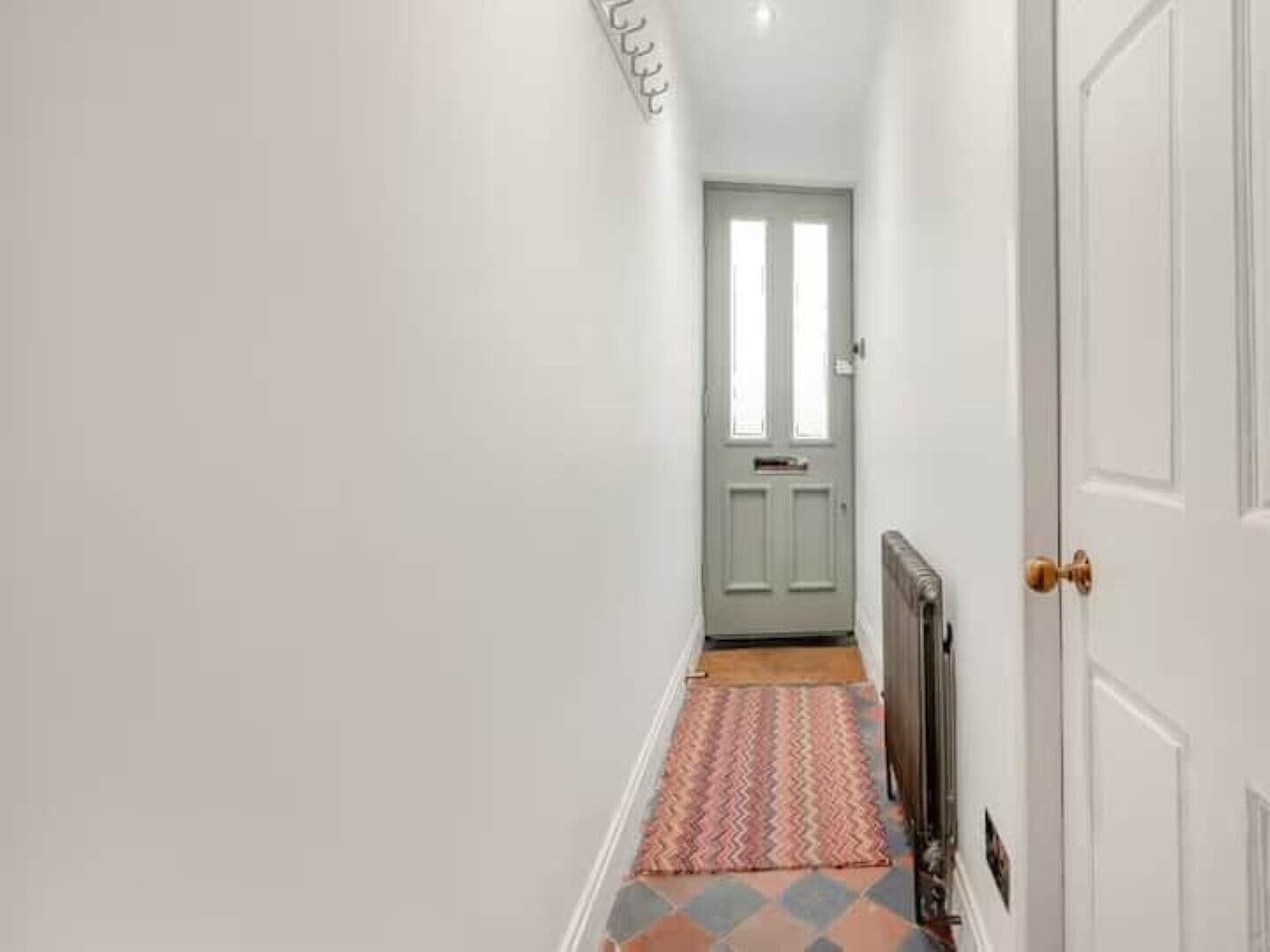 A narrow hallway with a patterned rug, a radiator, and a door with a light switch.