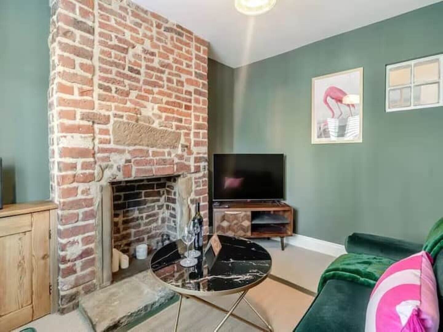 Una sala de estar con chimenea de ladrillo, un televisor de pantalla plana y un sofá verde.