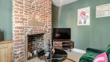 Una sala de estar con chimenea de ladrillo, un televisor de pantalla plana y un sofá verde.