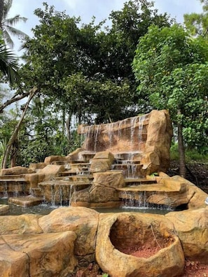 A natural rock waterfall with cascading water, surrounded by lush greenery and trees.