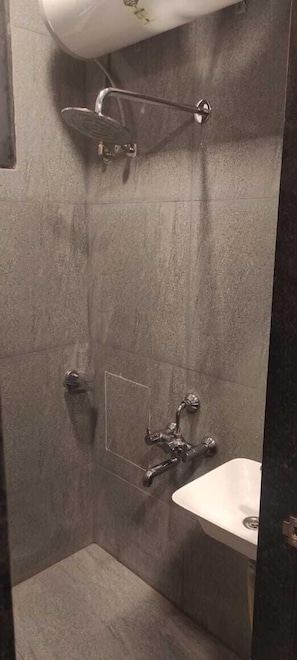 A small, tiled shower with a handheld showerhead and a wall-mounted faucet.