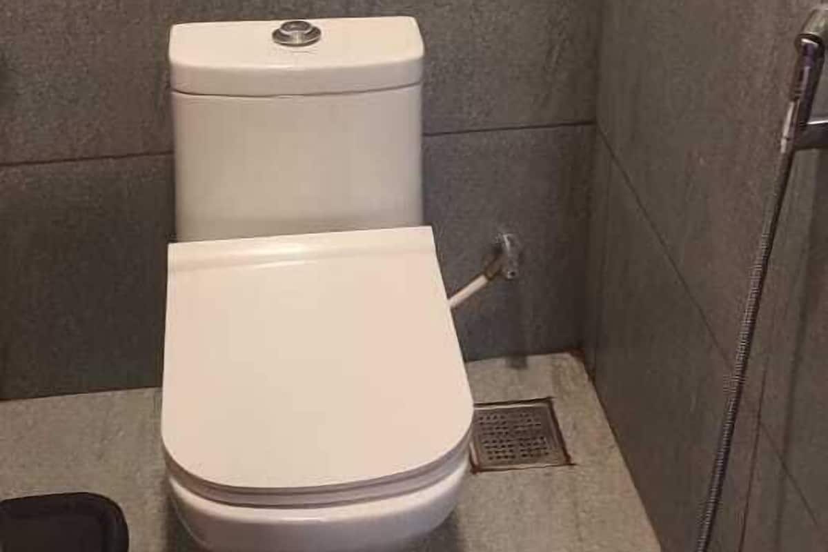 A small, tiled bathroom with a white toilet, a shower area, and a visible drain.