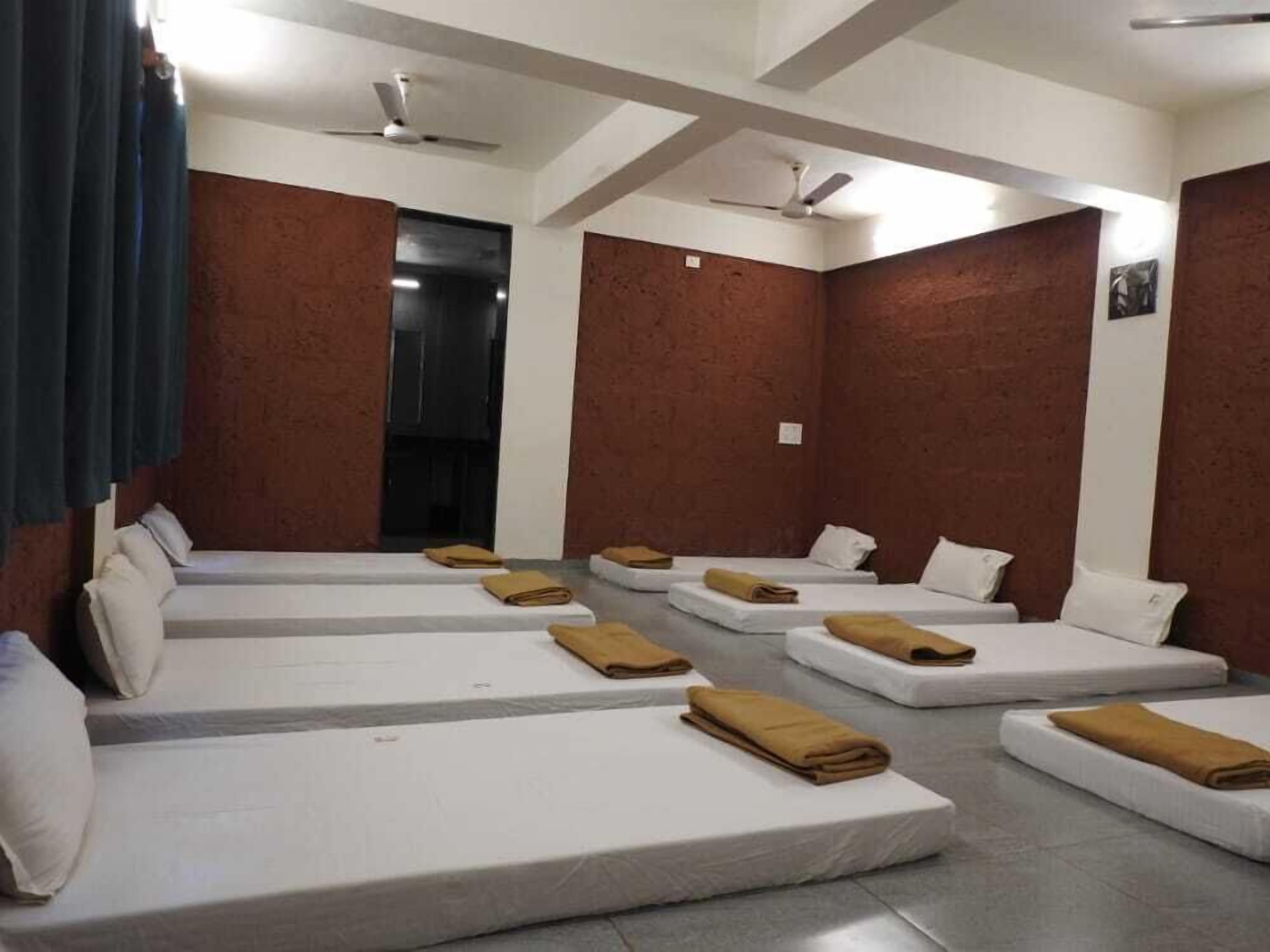 Ein Hotelzimmer mit mehreren nebeneinander stehenden Betten, jedes mit einem Kissen und einem Handtuch.