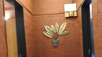 A hallway with a potted plant, a wall-mounted light fixture, and a small rock feature on the floor.