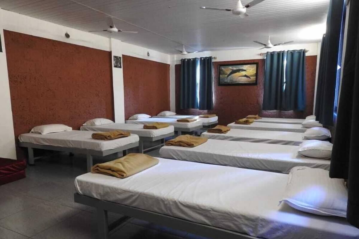 A hotel room with multiple single beds, each with a white mattress and a brown blanket.