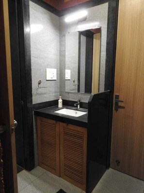 A bathroom with a black countertop sink, wooden cabinets, a mirror, and a door. - The Stream Resort (Shrivardhan)