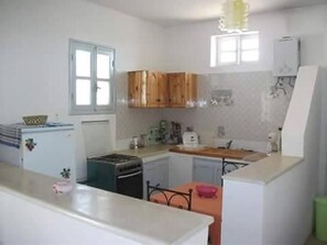 A compact kitchen with wooden cabinets, a refrigerator, and a stove. - DAR YOUSSEF (DJERBA MIDOUN)