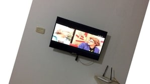 Un téléviseur fixé au mur, avec une prise électrique visible et une petite étagère en dessous.